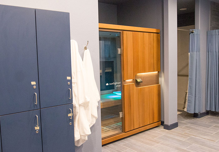 Women’s changing room with lockers, robes, and a sauna, featuring blue and wood accents. Women’s changing room with lockers, robes, and a sauna, featuring blue and wood accents.