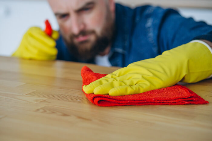 Man in yellow gloves cleaning a wooden surface with a red cloth, focusing on common hygiene habits.