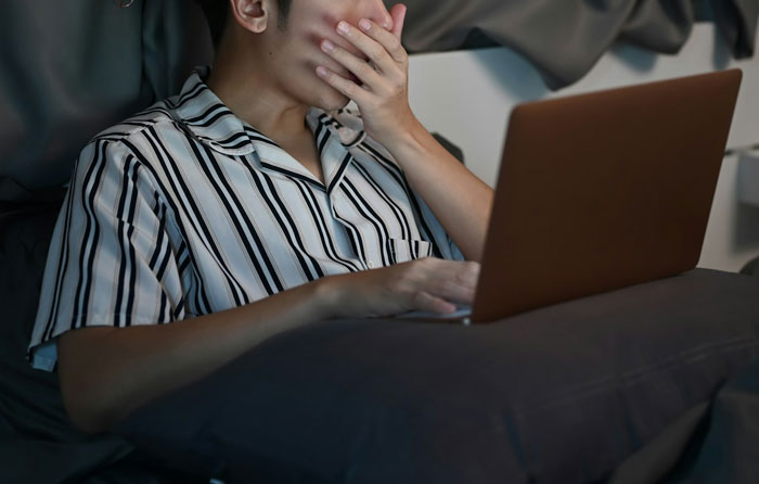 Man in striped pajamas looking shocked while using a laptop, expression of surprise. Man in striped pajamas looking shocked while using a laptop, expression of surprise.
