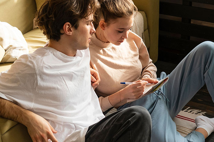 Young couple sitting together on a couch, discussing notes, highlighting moving out to live with her boyfriend. Young couple sitting together on a couch, discussing notes, highlighting moving out to live with her boyfriend.