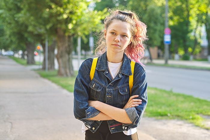 Teen girl with a denim jacket stands on a sidewalk, arms crossed, expressing defiance, related to pathological lies topic. Teen girl with a denim jacket stands on a sidewalk, arms crossed, expressing defiance, related to pathological lies topic.