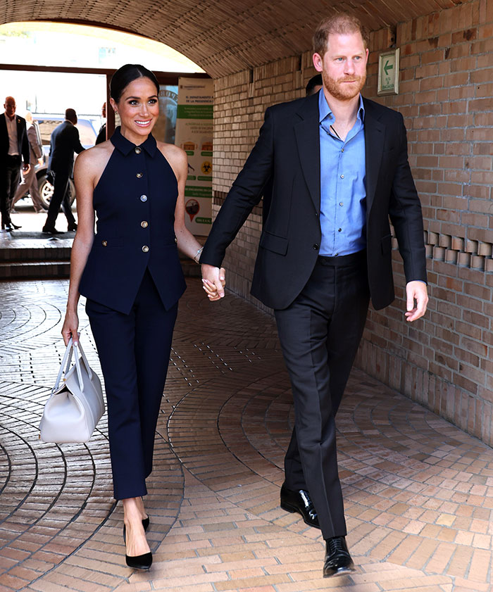 Royal couple holding hands in a formal setting, both in navy and black outfits, related to Hollywood news. Royal couple holding hands in a formal setting, both in navy and black outfits, related to Hollywood news.