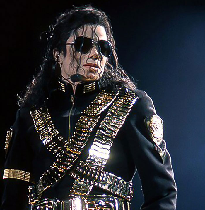 A performer in a dazzling black and gold outfit on stage, wearing sunglasses. A performer in a dazzling black and gold outfit on stage, wearing sunglasses.