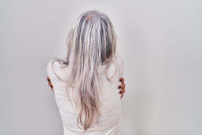 Individual with long gray hair facing away, highlighting genetic blessings and weaknesses.