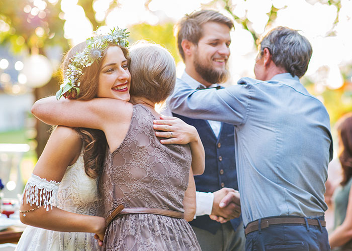 Bride and groom happily hugging guests at outdoor wedding, chosen date by MIL. Bride and groom happily hugging guests at outdoor wedding, chosen date by MIL.