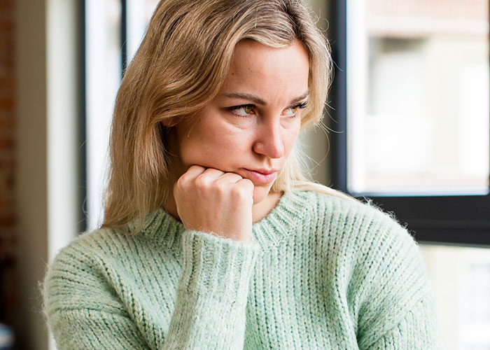 Woman in a light green sweater, sitting thoughtfully by a window, reflecting on wedding date decision. Woman in a light green sweater, sitting thoughtfully by a window, reflecting on wedding date decision.