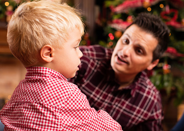 Man speaking to a young boy in plaid shirts, near a decorated Christmas tree, illustrating family conflict over renaming. Man speaking to a young boy in plaid shirts, near a decorated Christmas tree, illustrating family conflict over renaming.
