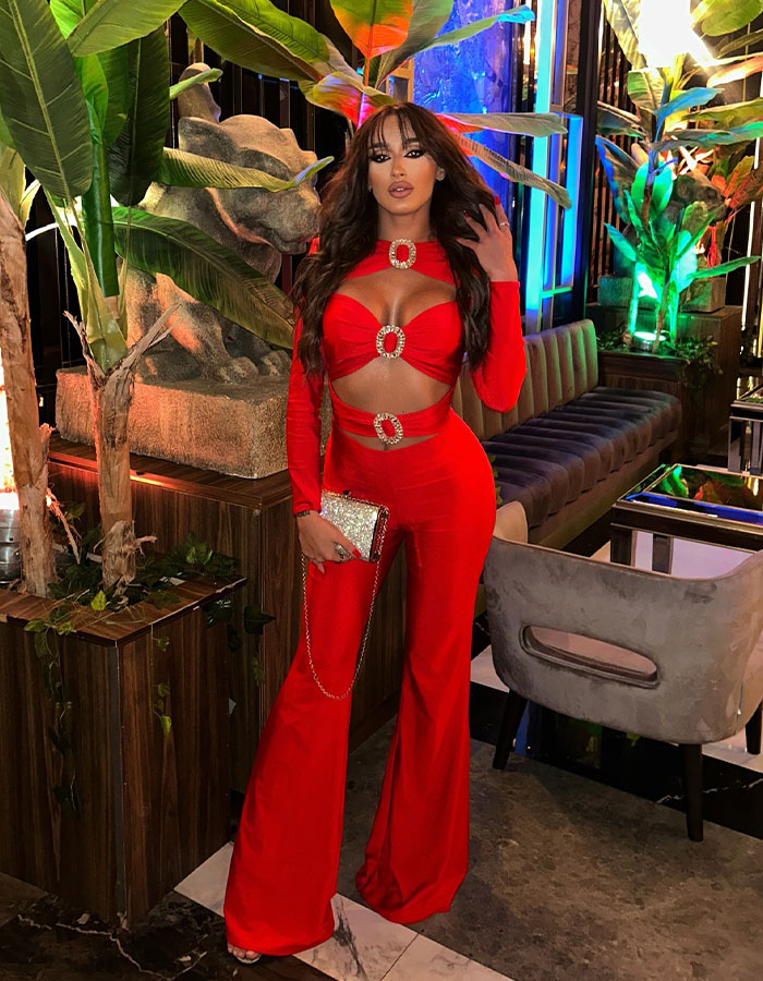Woman in a vibrant red outfit standing in a stylish venue with tropical decor. Woman in a vibrant red outfit standing in a stylish venue with tropical decor.