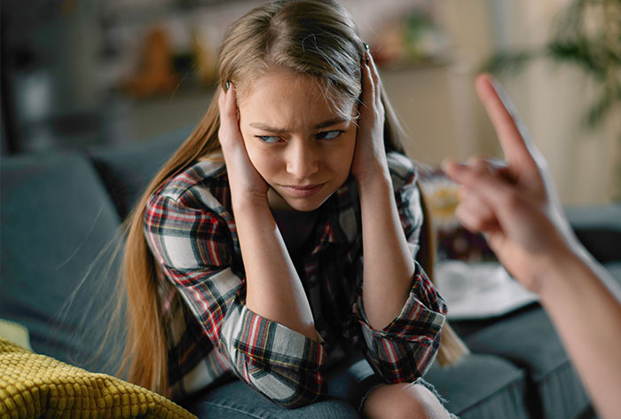 Teen girl looking frustrated, covering ears while being scolded, surrounded by home setting. Teen girl looking frustrated, covering ears while being scolded, surrounded by home setting.