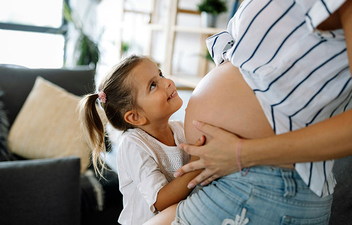 Child lovingly gazing at pregnant mom at home, highlighting growing up in family dynamics. Child lovingly gazing at pregnant mom at home, highlighting growing up in family dynamics.