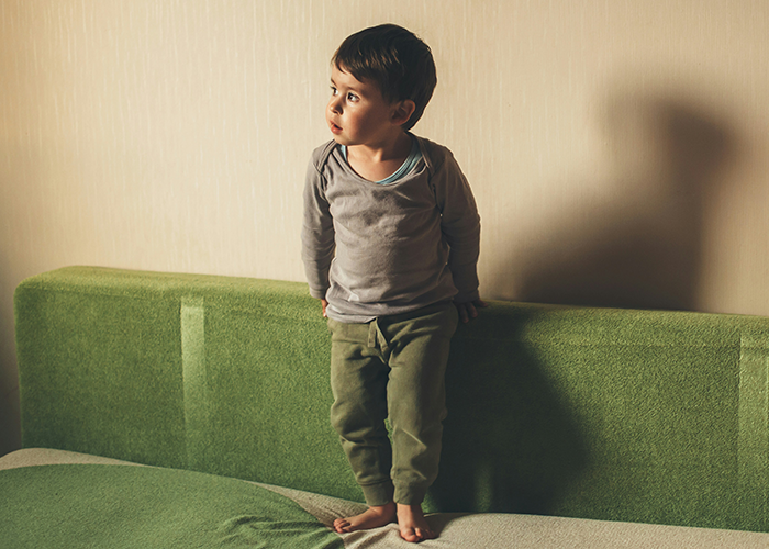 Young boy in a thoughtful pose on a green couch, highlighting family dynamics and strict parenting decisions. Young boy in a thoughtful pose on a green couch, highlighting family dynamics and strict parenting decisions.