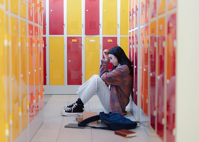 Teen sitting in a school hallway near lockers, looking upset and alone. Teen sitting in a school hallway near lockers, looking upset and alone.