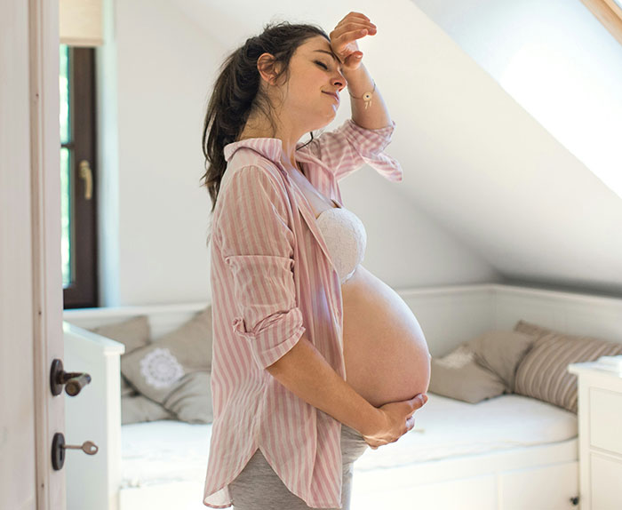 Pregnant woman stands thoughtfully in a cozy bedroom, touching her belly. Pregnant woman stands thoughtfully in a cozy bedroom, touching her belly.