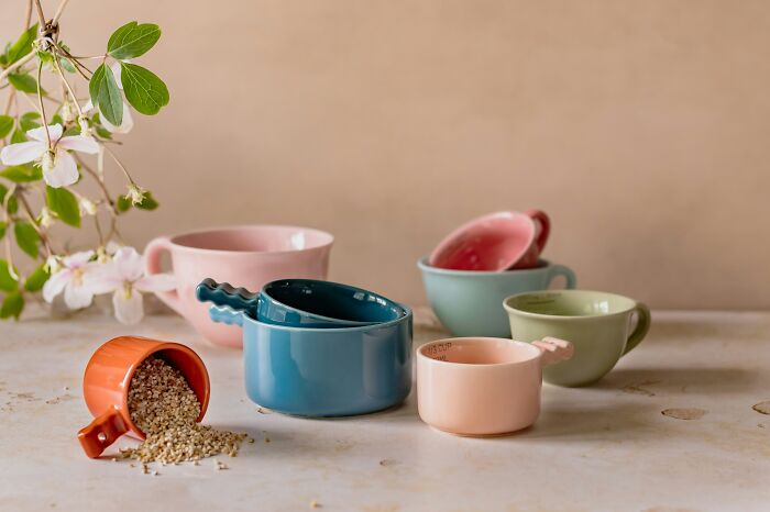 Multi-functional colorful measuring cups on a table with scattered seeds, embodying minimalism and versatility.