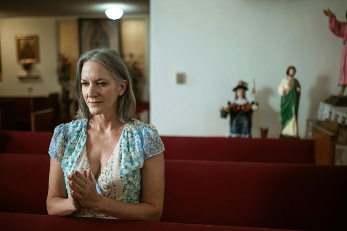 Religious MIL praying in a church pew, with statues in the background. Religious MIL praying in a church pew, with statues in the background.