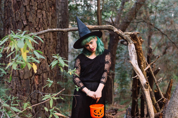 Woman dressed as a witch for Halloween, holding a pumpkin bucket, standing in a forest. Woman dressed as a witch for Halloween, holding a pumpkin bucket, standing in a forest.