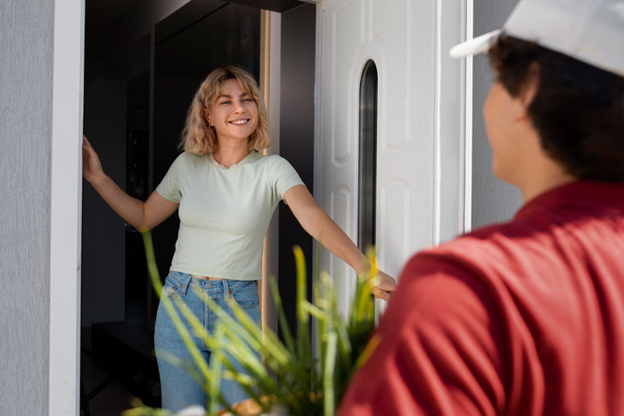 Neighbor receiving a package at the door while smiling, related to neighborhood loans topic. Neighbor receiving a package at the door while smiling, related to neighborhood loans topic.