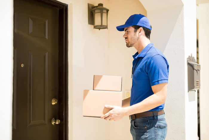 Delivery person holding packages at a front door, wearing a blue cap and shirt, part of neighborhood loans context. Delivery person holding packages at a front door, wearing a blue cap and shirt, part of neighborhood loans context.