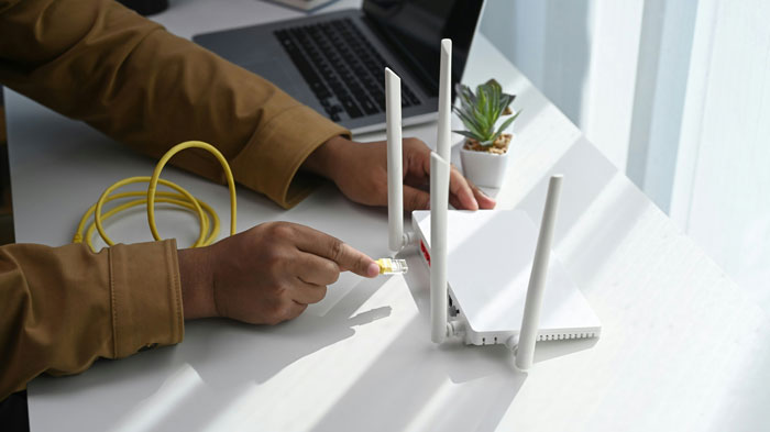 Person connecting ethernet cable to router, surrounded by a laptop and plant; concept of wifi password issues. Person connecting ethernet cable to router, surrounded by a laptop and plant; concept of wifi password issues.