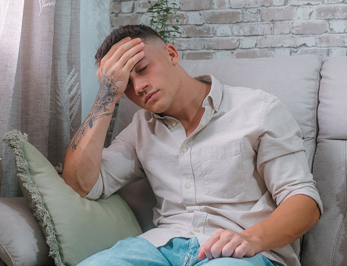 Man sitting distressed in living room, wearing a light shirt, tattoo on forearm, related to backyard wedding dispute. Man sitting distressed in living room, wearing a light shirt, tattoo on forearm, related to backyard wedding dispute.