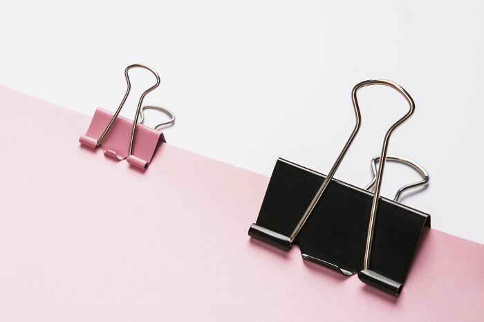 Two binder clips on pink paper symbolizing multifunctional items for minimalism.
