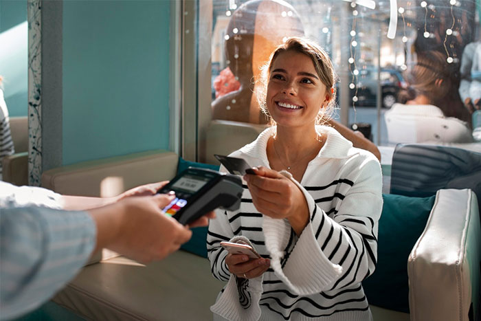 Smiling woman pays with a card in a cafe, discussing "pay it forward" chain etiquette. Smiling woman pays with a card in a cafe, discussing "pay it forward" chain etiquette.
