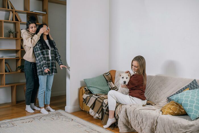 Two friends play a game while another person with a dog relaxes on the couch, illustrating social rules people ignore.