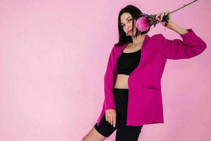 Person in pink blazer holding flower against pink background, illustrating recent fashion trends people hate.