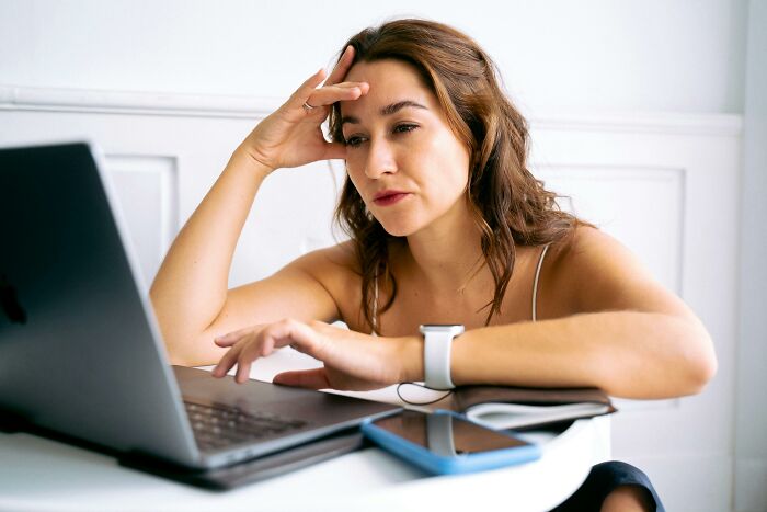 A woman experiencing work struggles, looking frustrated while working on a laptop at a desk.