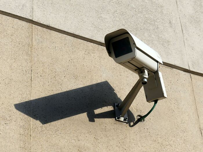 Security camera mounted on a beige wall, symbolizing work-struggles related to surveillance in the workplace.
