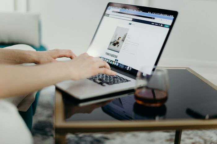 Person typing on a laptop, showcasing a webpage about brilliant life hacks, next to a coffee glass on a table.