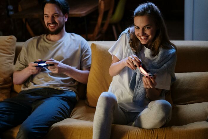 Two people on a couch having fun, smiling and holding game controllers, depicting a relaxed moment after office hours.
