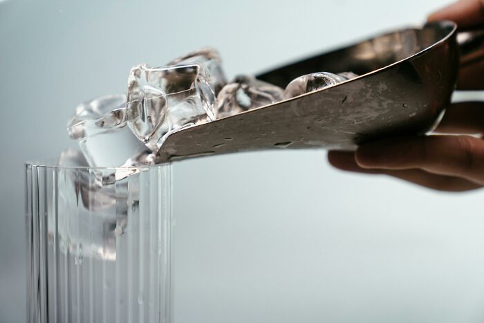 Pouring ice cubes into a glass using a metal scoop, illustrating a common work-struggles scenario with simple tasks.