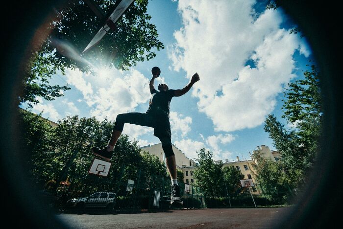 Person playing basketball outdoors, showcasing genetic blessings in a dynamic leap towards the hoop.