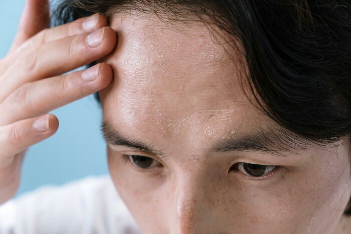 Person sweating and touching forehead, reflecting work-struggles in a close-up shot against a light blue background.