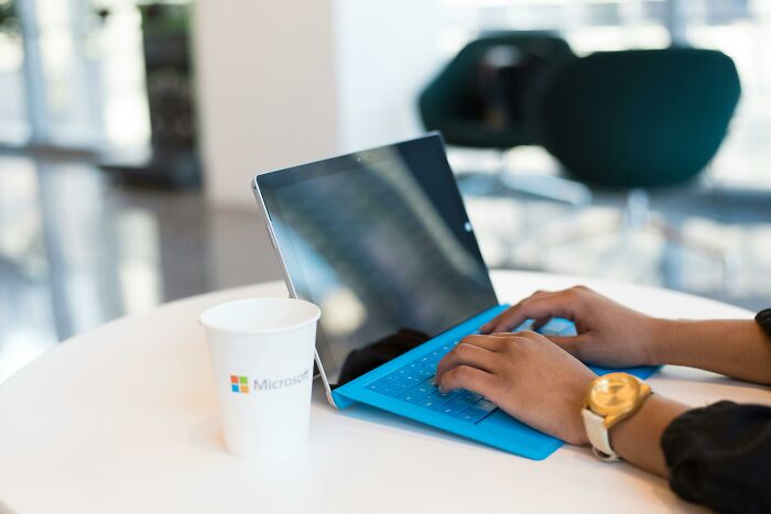 Hands typing on a blue keyboard in an office setting with a Microsoft cup, capturing office humor moments.