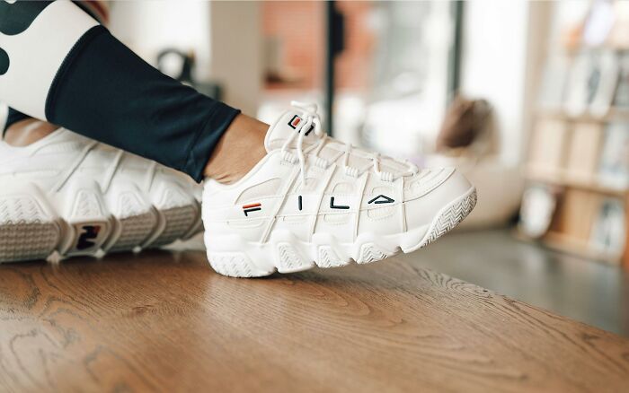 White Fila sneakers on a wooden floor, capturing recent fashion trends people hate.