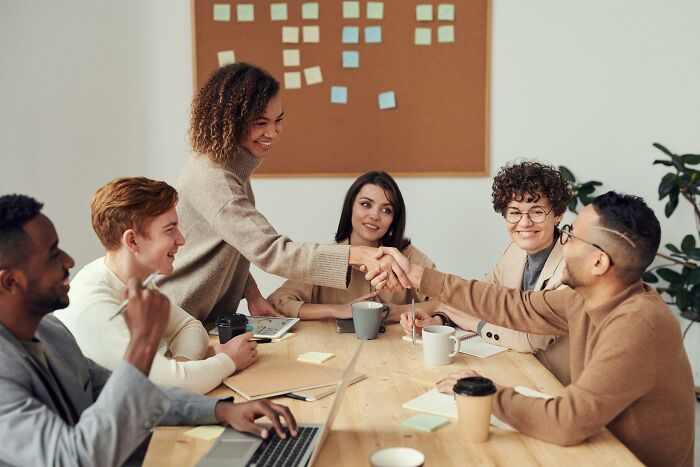 People in a meeting room, discussing and shaking hands, emphasizing social rules people often ignore in professional settings.
