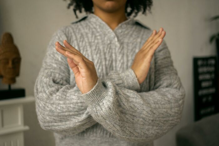 Person in a gray sweater crossing arms in front, symbolizing ignored social rules indoors.