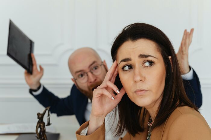 Man raising hands in frustration while woman considers work skills people lack in an office setting.