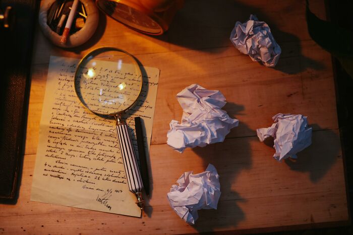 Magnifying glass and crumpled papers on a desk, suggesting a detective scene related to famous characters. Magnifying glass and crumpled papers on a desk, suggesting a detective scene related to famous characters.