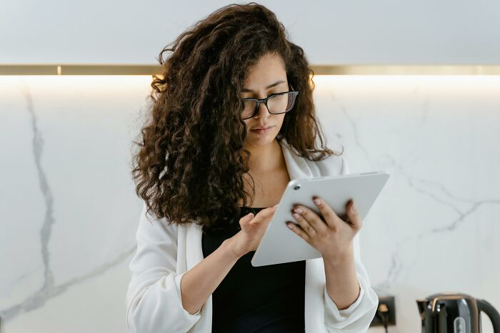 Person using a tablet with curly hair and glasses, implementing brilliant life hacks in a modern kitchen setting.