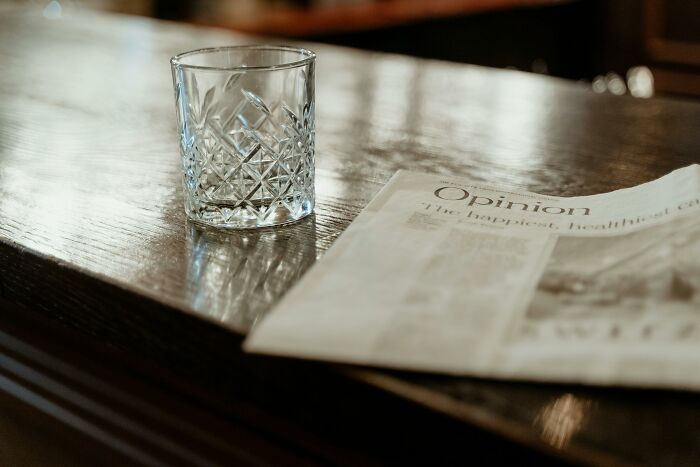 Crystal glass on wooden table beside a newspaper, evoking a quiet office setting.