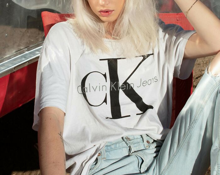 Person wearing a Calvin Klein logo tee and jeans, representing recent fashion trends people hate.