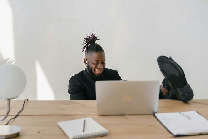 Person smiling, lounging at desk with laptop, illustrating work-struggles in a relaxed office environment.
