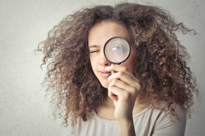 Woman holding a magnifying glass to her eye, illustrating attention to detail for a reality check quiz. Woman holding a magnifying glass to her eye, illustrating attention to detail for a reality check quiz.
