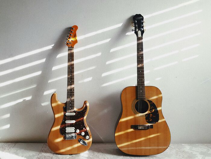 Two guitars, electric and acoustic, rest against a wall, casting striped shadows, illustrating general music knowledge. Two guitars, electric and acoustic, rest against a wall, casting striped shadows, illustrating general music knowledge.