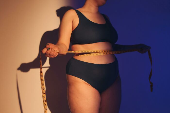 Person measuring waist with a tape, highlighting genetic blessings and weaknesses in body image.