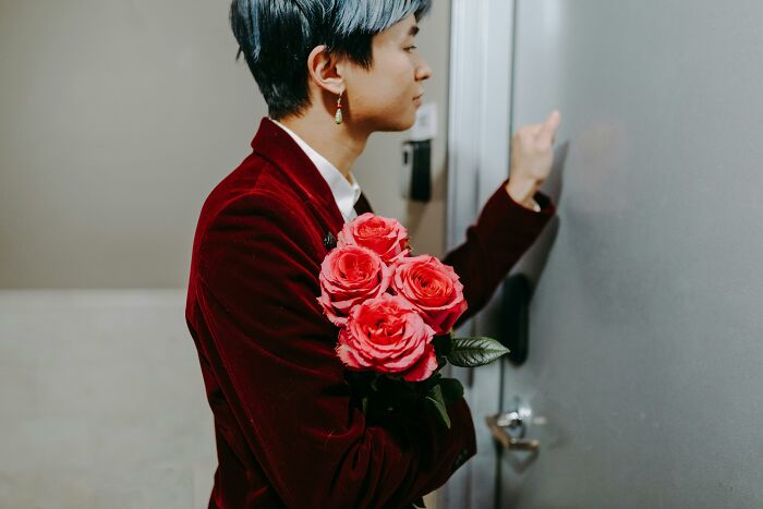Person knocking on a door with roses in hand, ignoring social rules, in a red velvet jacket.