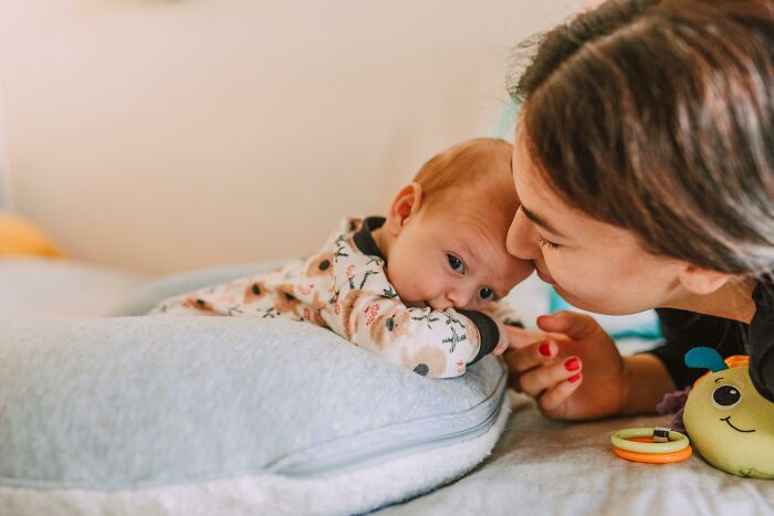 A mother gently kisses her baby's forehead while the baby lies on a pillow, illustrating tender moments people often ignore.